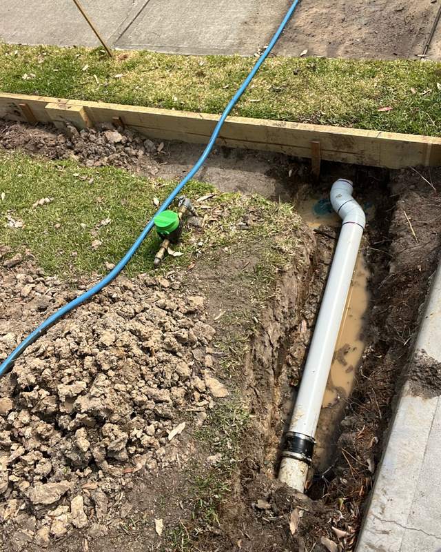 New white stormwater pipe laid in a trench beside a lawn