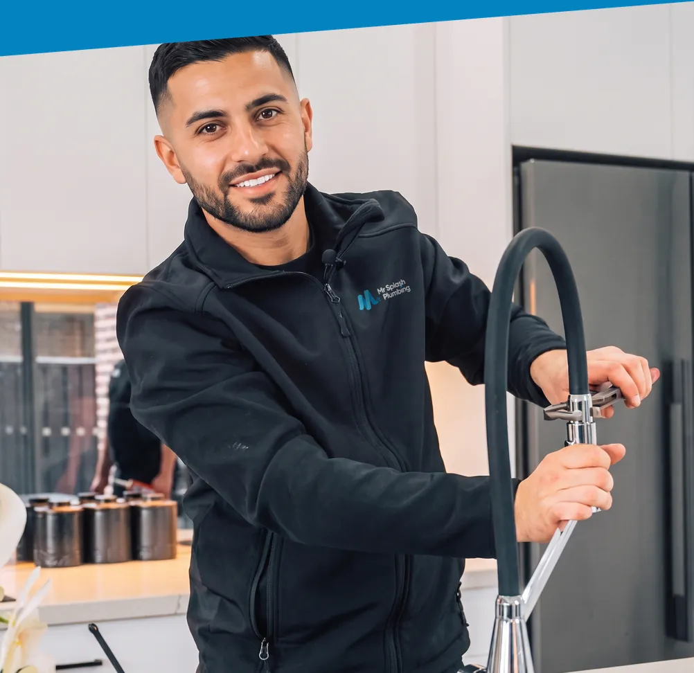 Plumber in a Mr Splash Plumbing jacket fixing a kitchen mixer tap