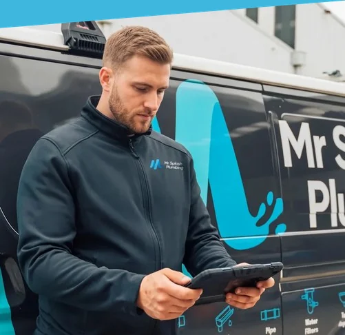 Plumber in a Mr Splash Plumbing jacket checking a tablet beside a Mr Splash van