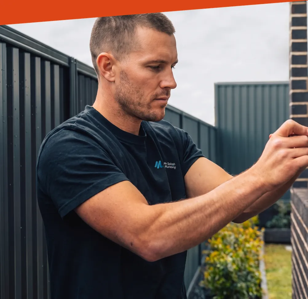 Plumber in a Mr Splash Plumbing t-shirt working on an outdoor fitting