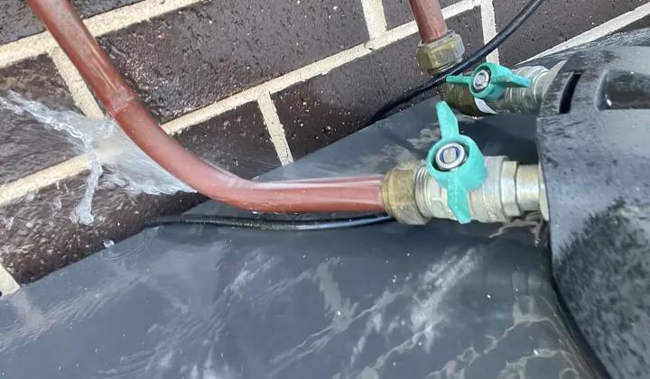 Water spraying from a split copper pipe beside a brick wall