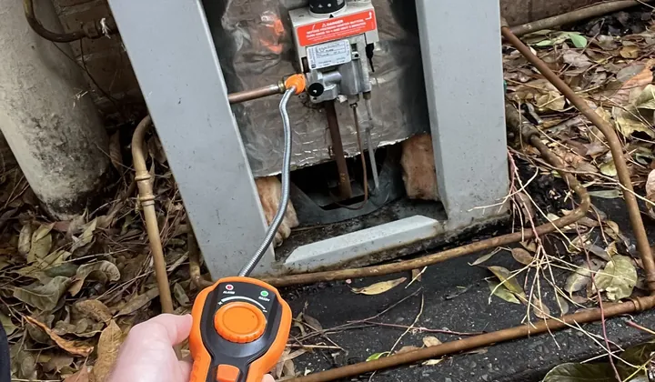 Plumber holding a gas leak detector at the gas control of a hot water system