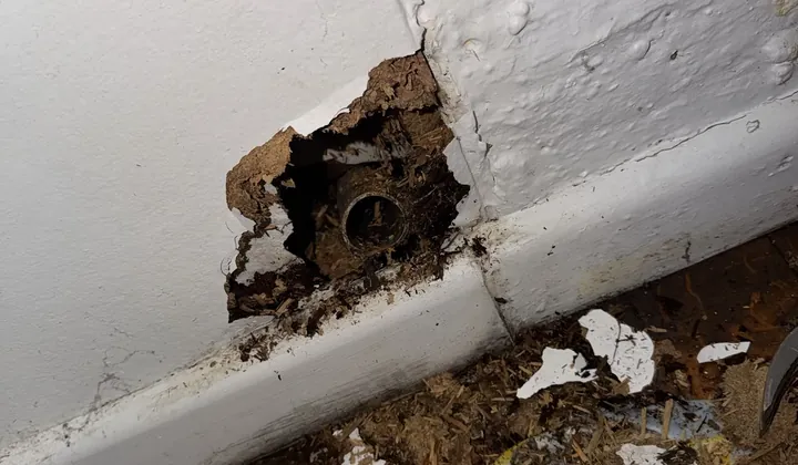 Wall opened at the skirting board to expose a leaking pipe fitting