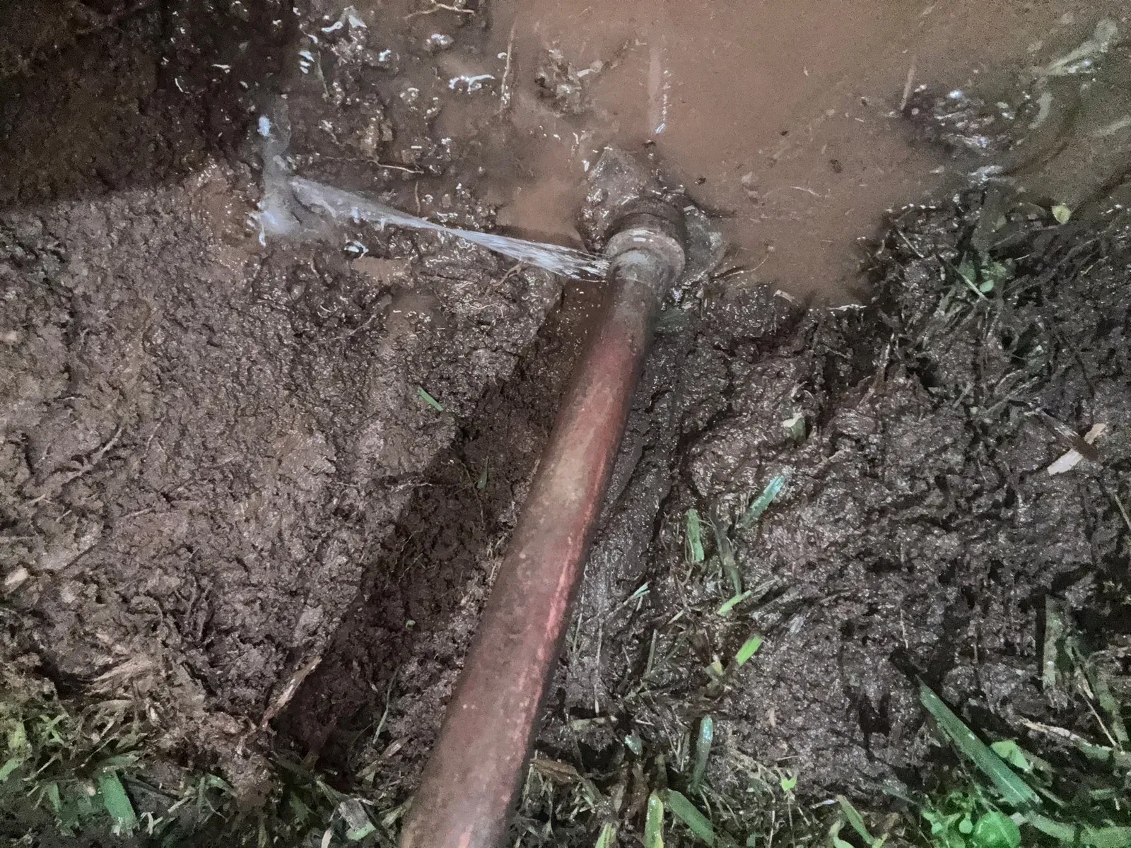 Water spraying from a leaking copper water pipe dug out of a lawn at night