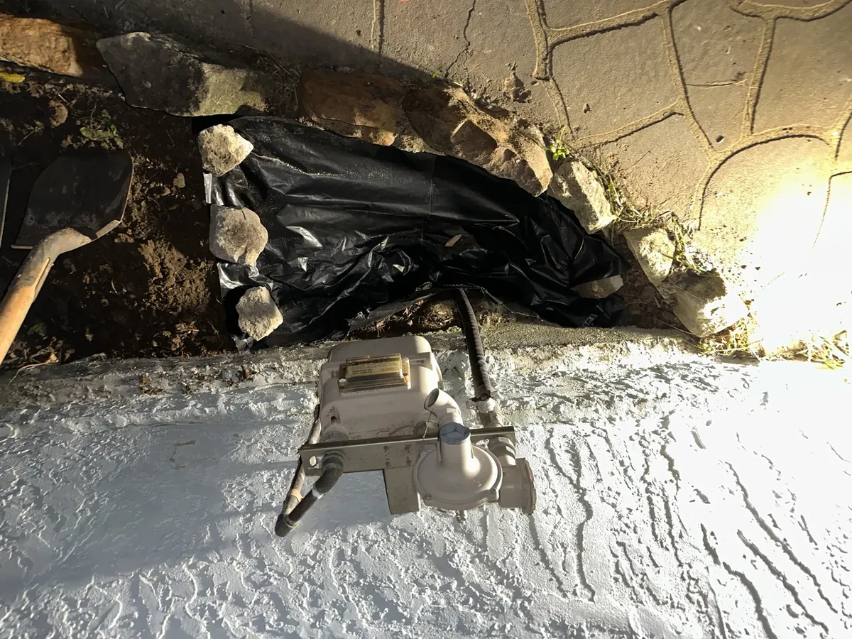 Gas meter with the ground dug out beside it, lit by work lights at night