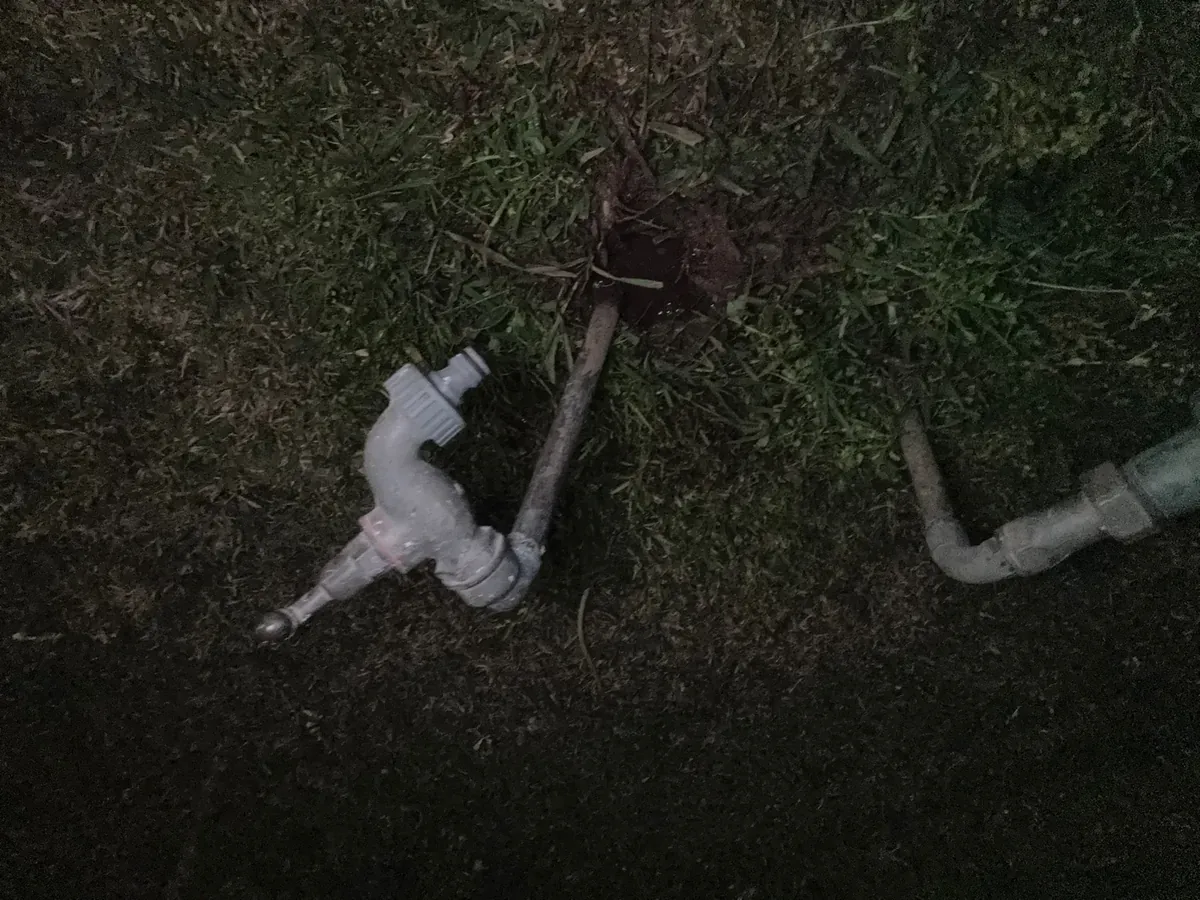 Broken outdoor tap and pipe lying on a lawn at night