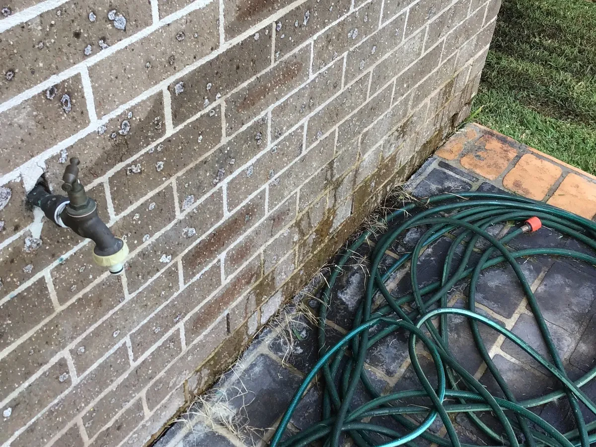 Outdoor garden tap on a brick wall with a coiled hose below