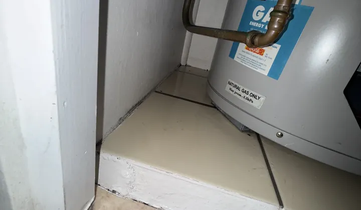 Base of a natural gas storage tank and its copper pipes on a tiled step inside a cupboard in Tempe
