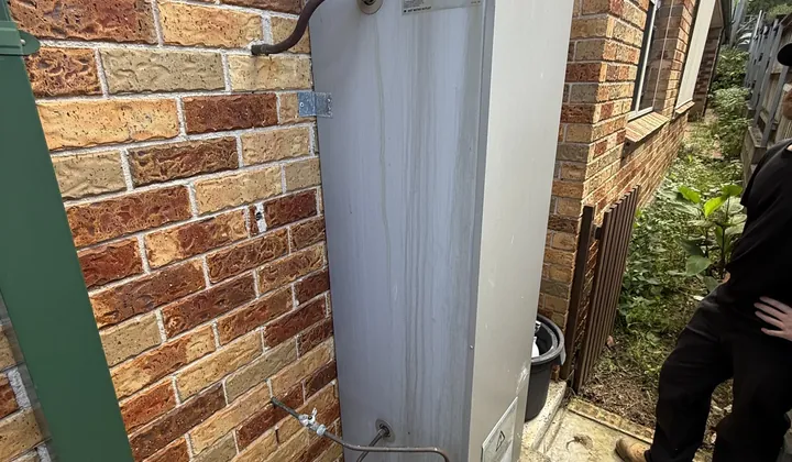 Old gas storage hot water unit with its flue cowl against a brick wall in Allambie Heights