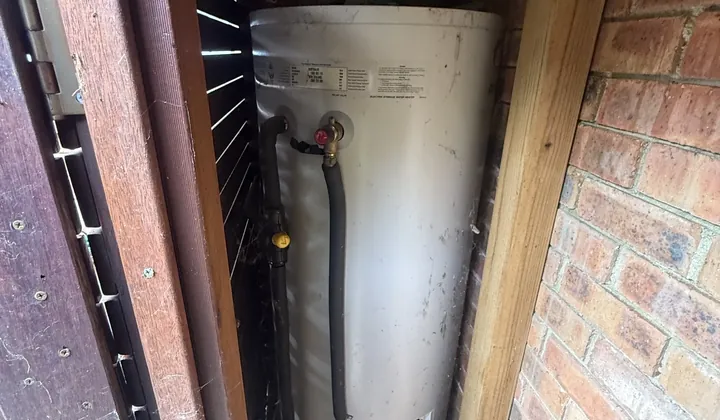Electric hot water tank inside a timber enclosure against a brick wall in Cremorne