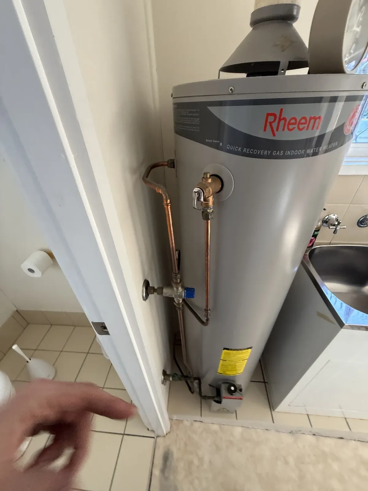 Aquamax Hot Water Sydney - Indoor gas storage hot water unit with a flue hood on top and copper pipes in Tempe