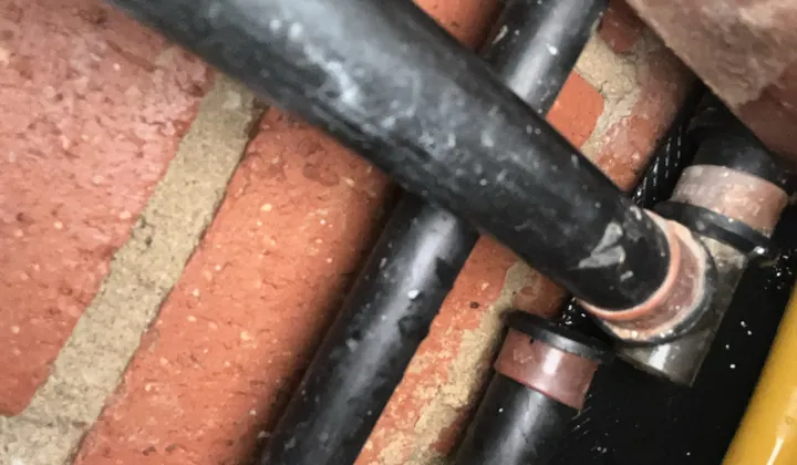 Lagged and copper hot water pipes running across a brick wall in Oran Park