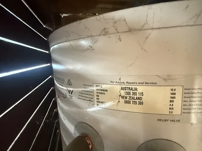 Data plate on an electric hot water tank in a cupboard showing 250 litres