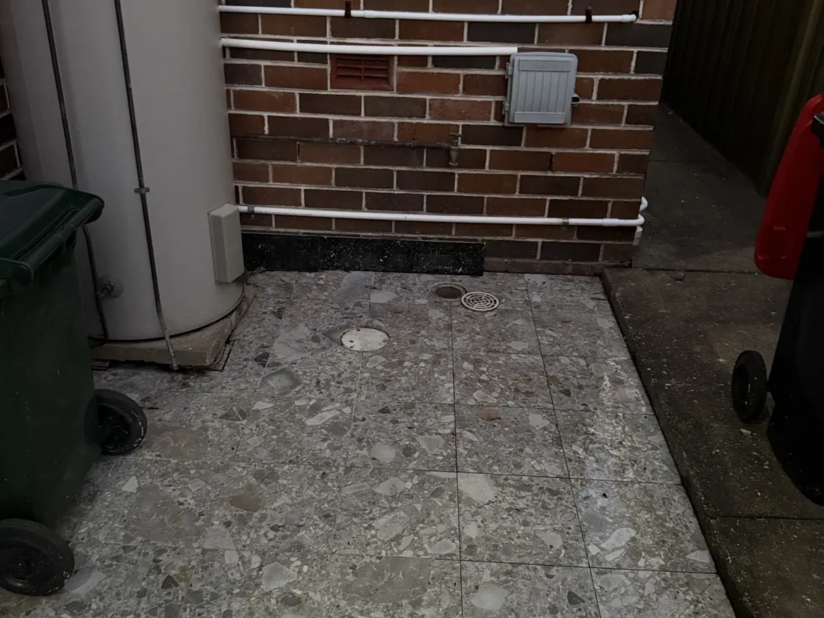 Tiled side courtyard with the floor drain and downpipe beside the hot water unit in Kingsgrove