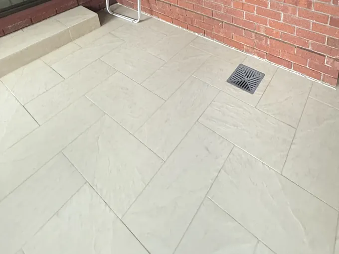 Floor grate set into the tiled courtyard beside a brick wall in Penshurst