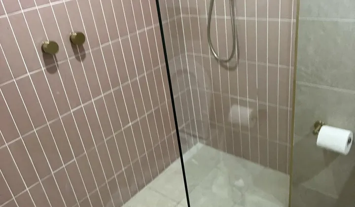 Walk-in shower with pink tiles, a brass rail shower and a brass strip drain across the floor in Strathfield