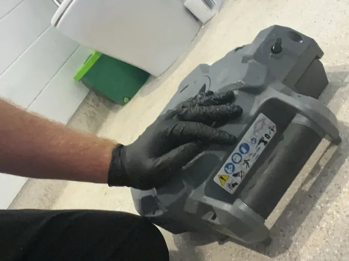 Gloved hand on the drum of a drain cleaning machine on a bathroom floor beside the toilet in Westmead