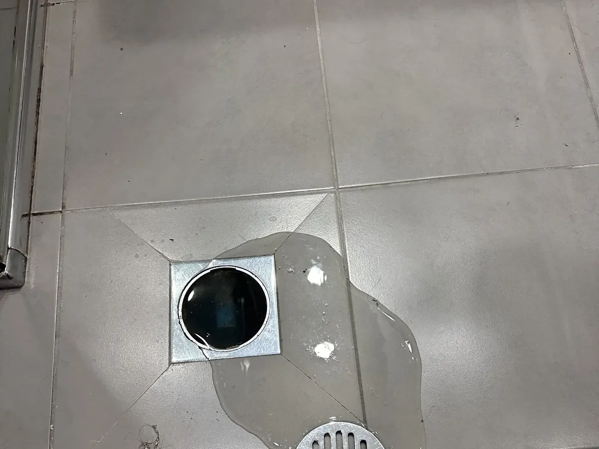 Bathroom floor waste with its grate lifted off and water pooled around it on grey tiles in Rouse Hill