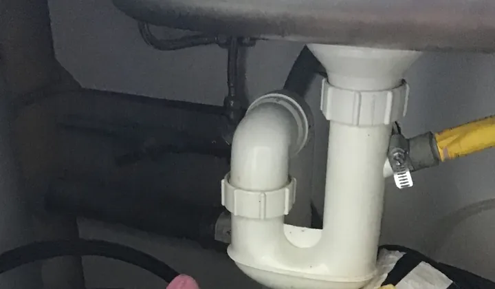 White plastic trap and waste pipe under a blocked stainless kitchen sink in Centennial Park