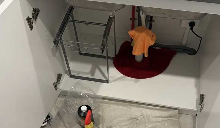 Waste pipes taken off a double kitchen sink and laid in one bowl, with a plunger on a drop sheet below, in Botany