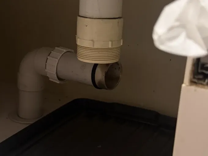 Sink trap removed under a kitchen cupboard, leaving the open waste pipe above a drip tray, in Erskineville