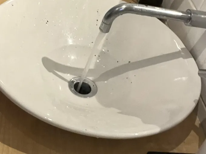 Water running straight down the waste of a white vessel basin on a timber vanity in Erskineville