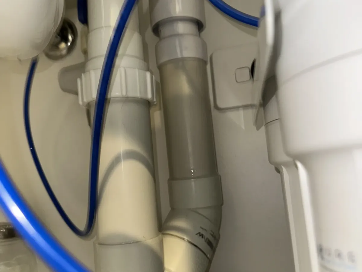 White and grey PVC waste pipes under a kitchen sink, with an appliance drain hose and blue filter tubing, in Erskineville
