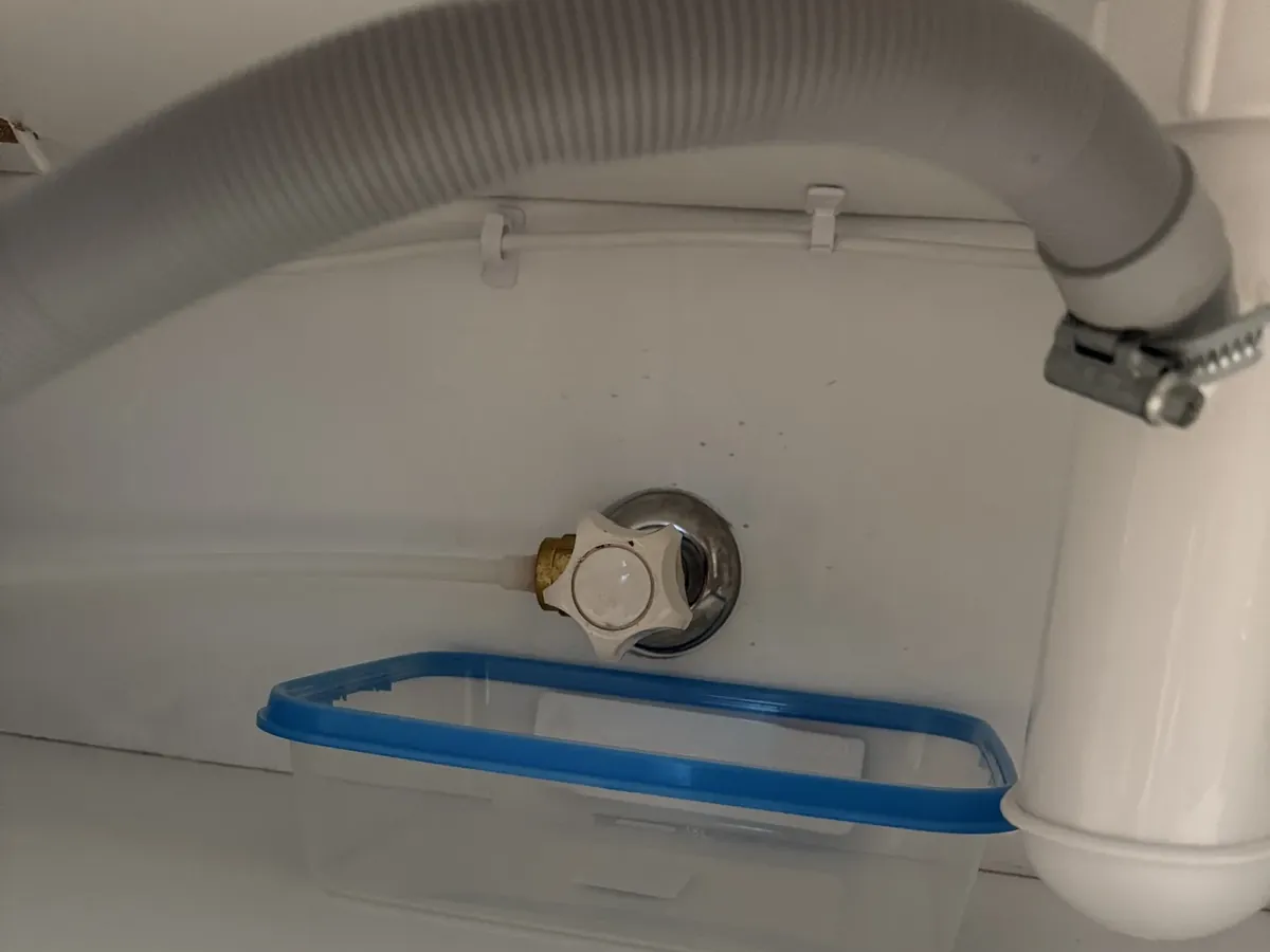 Grey appliance drain hose clamped onto the waste pipe under a sink in Rosebery