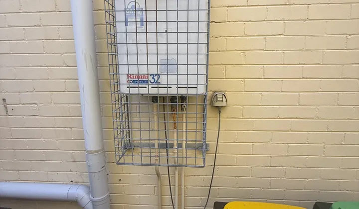 Continuous flow gas hot water unit in a wire cage on a brick wall in Oatley