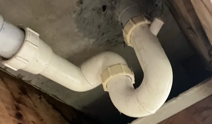 White waste pipe and trap under a concrete slab, seen through an opening cut in a ceiling in Bankstown
