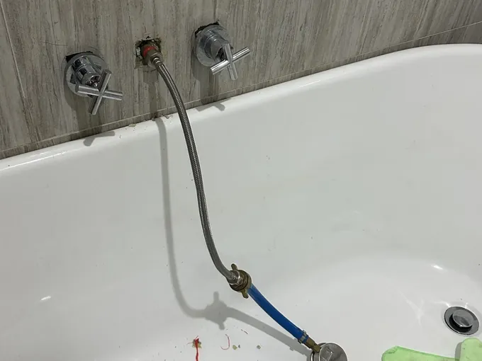 Bath spout taken off and a braided hose connected to the outlet in the wall, between the bath taps, in Condell Park