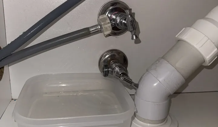 Washing machine hoses on laundry wall taps with a container catching water below in Harrington Park