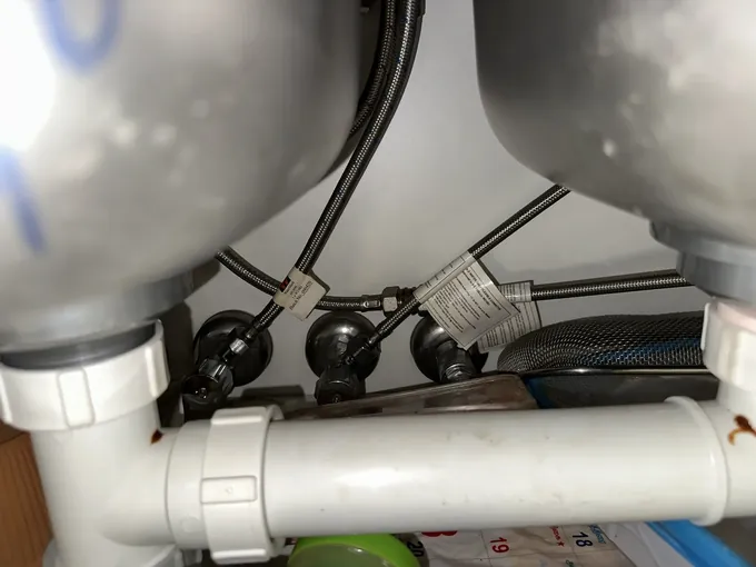 Braided flexi hoses with their product labels still attached under a double kitchen sink in Seven Hills