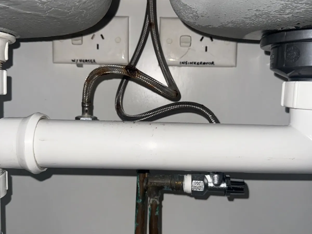 Rusted braided flexi hose under a double kitchen sink in Haberfield