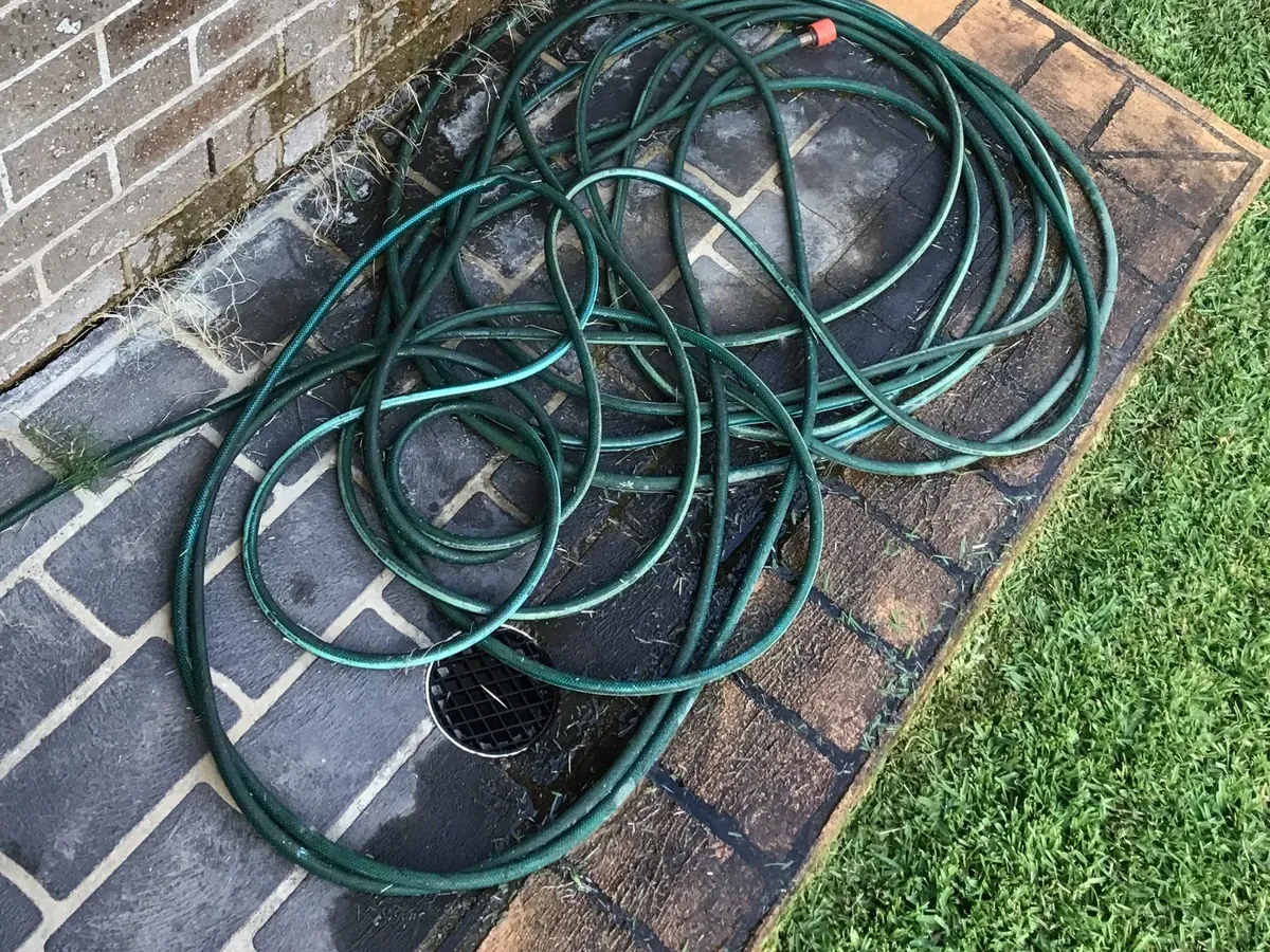Garden hose coiled on wet paving beside the brick wall of the house in Glenmore Park
