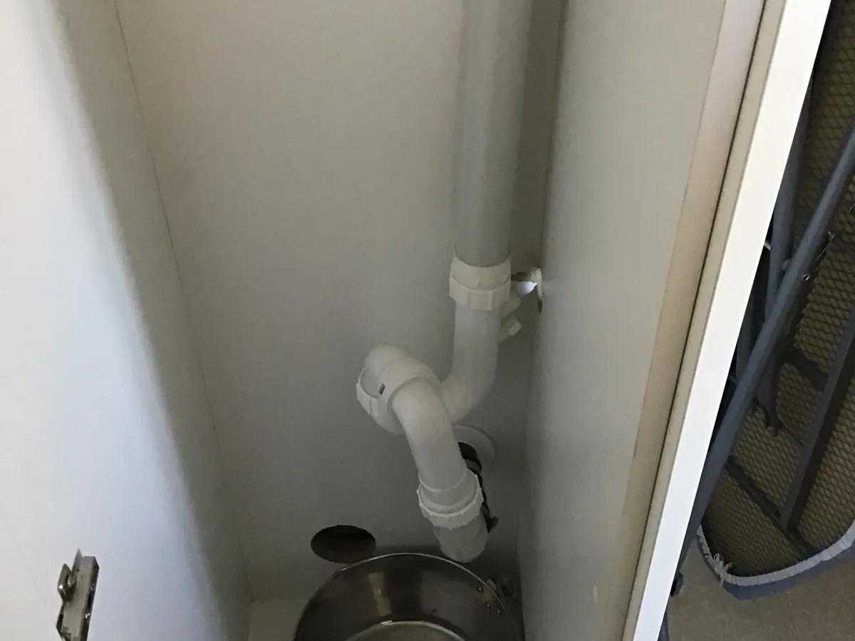 Saucepan catching drips under a leaking pipe inside a kitchen cupboard in Bondi Beach