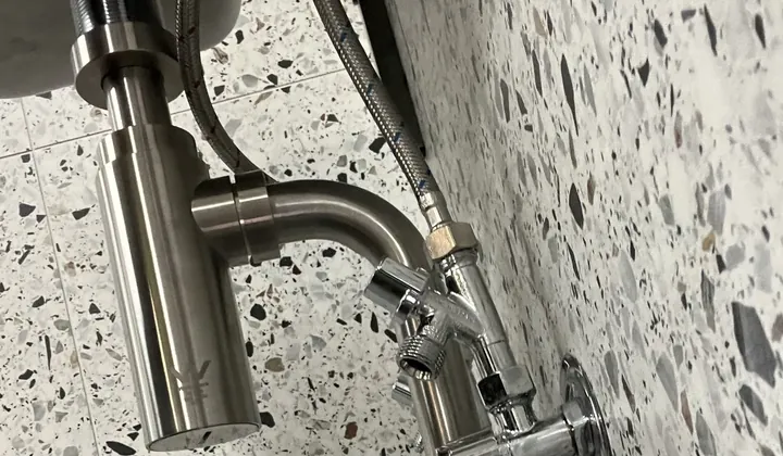 Stainless basin waste and isolation valves on a terrazzo tiled wall in a Chullora washroom