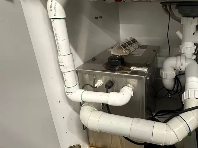 Under-sink sullage pump and white waste pipes below a stainless sink at a workshop in Seven Hills