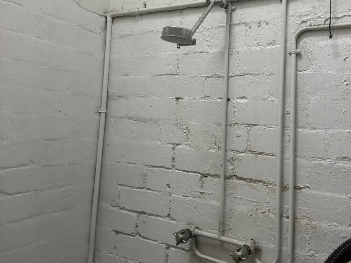 Shower taps and exposed pipework on a painted brick wall at a business in Alexandria