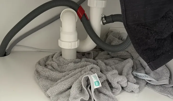 Grey dishwasher drain hose looped up to the sink trap, with towels below it, in Spring Farm