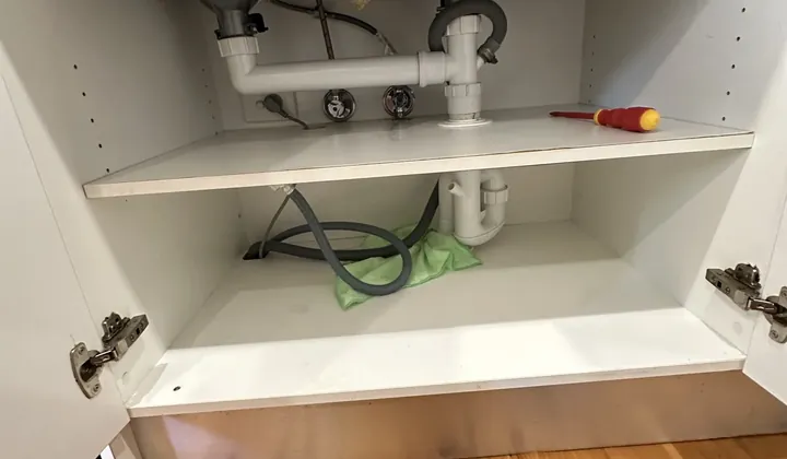 Sink wastes, water valves and a dishwasher hose under a double sink mid-swap in Woolloomooloo