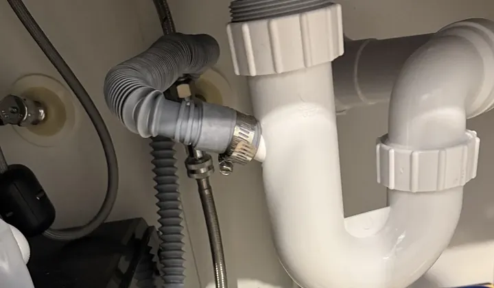 Drain hose clamped to a white trap beside a braided water line under a sink in Surry Hills