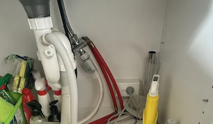 Dual water valve with red hoses and a dishwasher hose under a kitchen sink in Glebe
