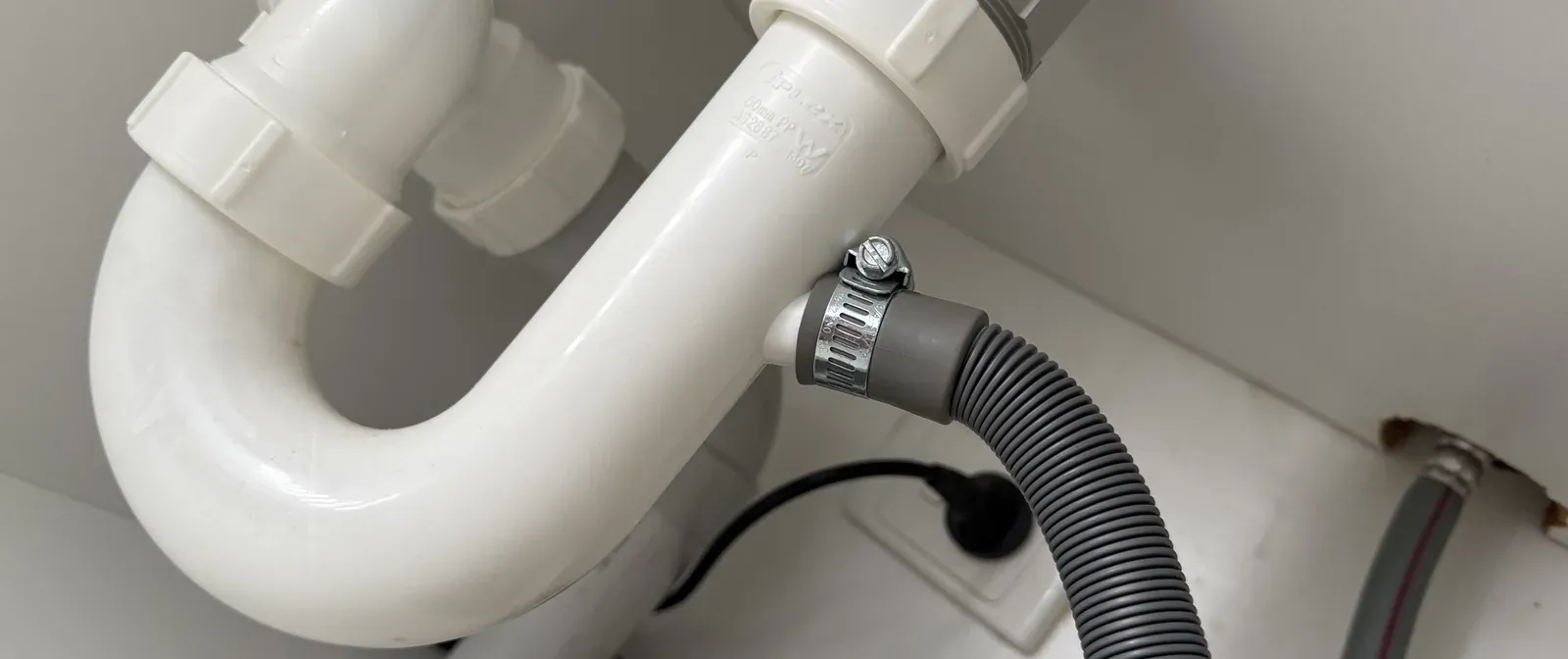 Dishwasher drain hose clamped onto the spigot of a sink trap under a kitchen sink in Roselands