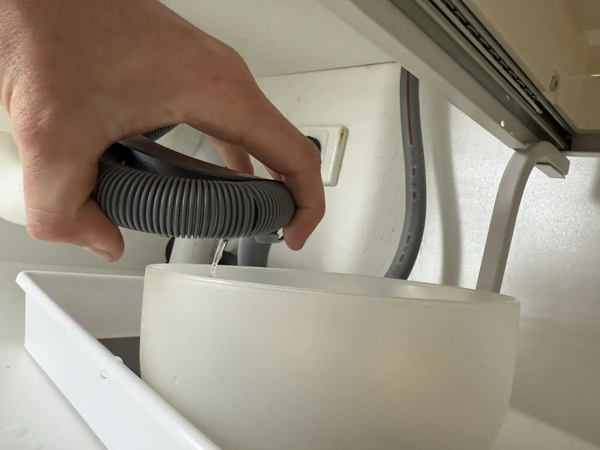 Plumber holding a dishwasher drain hose as water runs out into a bowl in Roselands