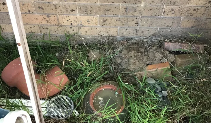 Old clay bend and a lifted grate beside a gully full of dirty water in South Penrith