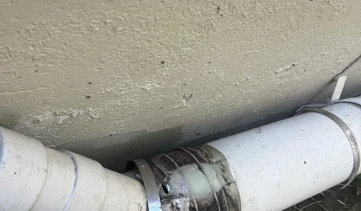 Split rubber coupling on a PVC drain pipe along a rendered house wall in Newtown