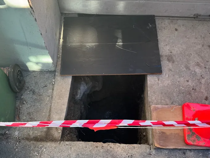 Square hole cut through a concrete slab behind red and white barrier tape in Newtown