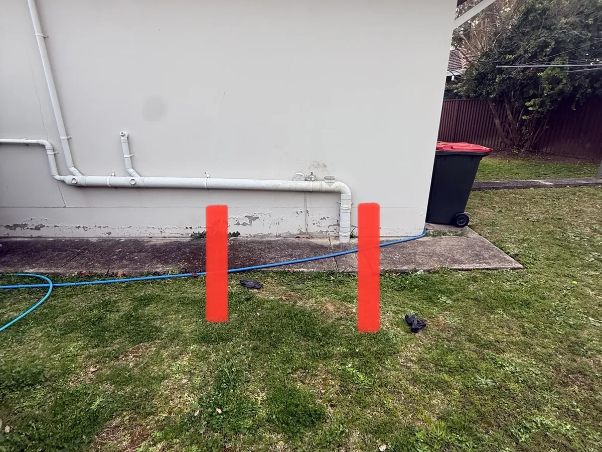 White waste pipes along a house wall with two red markers drawn over the lawn in Toongabbie