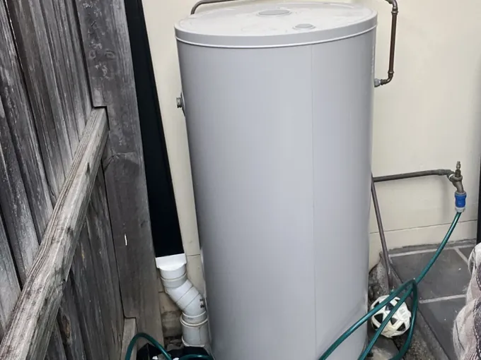 Grey electric hot water tank on a paver between a timber fence and a rendered wall in Macquarie Fields